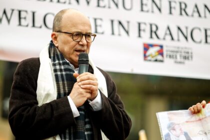 a man speaking into a microphone in front of a sign