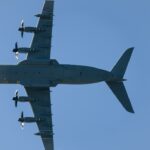 Four-engine turboprop aircraft flying in clear blue sky.
