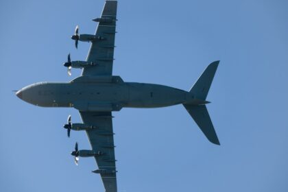Four-engine turboprop aircraft flying in clear blue sky.