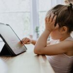 girl in white tank top using black tablet computer