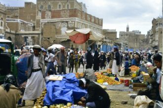 Bustling marketplace with people and goods in a historic city.