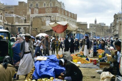 Bustling marketplace with people and goods in a historic city.