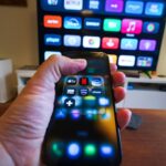 Hand holding smartphone controlling smart TV apps