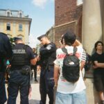 Police officers stand near civilians on a street.