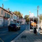 Car driving down a street with buildings and bus stop.