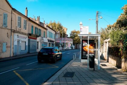 Car driving down a street with buildings and bus stop.