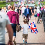 selective focus photography of boy holding U.K. flag walking on pathway full of people