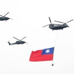 A group of military helicopters flying over a flag
