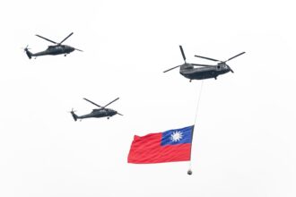 A group of military helicopters flying over a flag