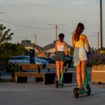 Two women riding electric scooters on a sunny day.