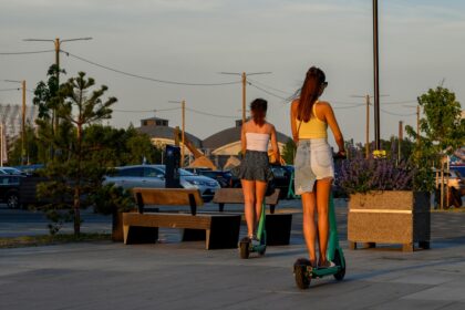 Two women riding electric scooters on a sunny day.