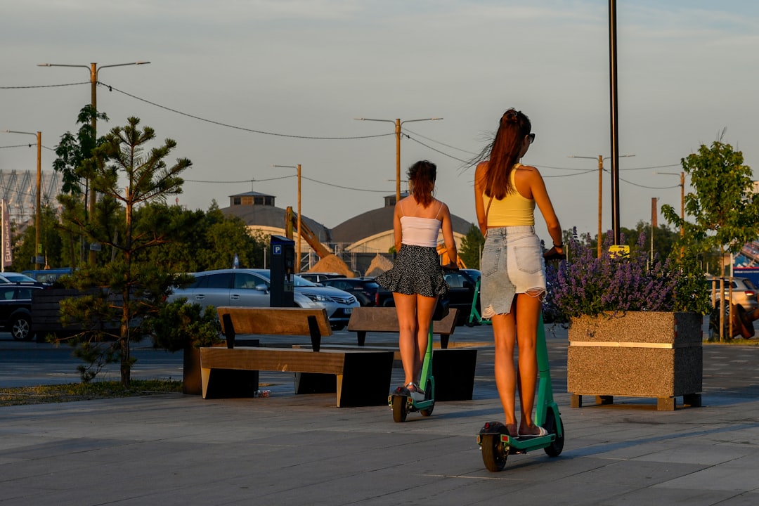 Two women riding electric scooters on a sunny day.