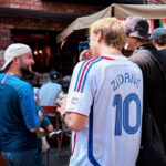 Men talking outdoors, one wearing a zidane soccer jersey.