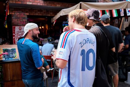 Men talking outdoors, one wearing a zidane soccer jersey.