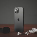 A smartphone, a smartwatch, and wireless earbuds on a wooden surface