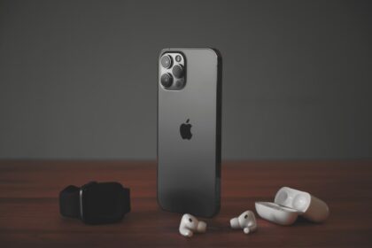 A smartphone, a smartwatch, and wireless earbuds on a wooden surface
