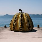 Giant yellow polka-dot pumpkin sculpture on a pier