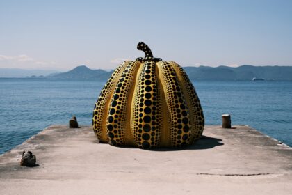 Giant yellow polka-dot pumpkin sculpture on a pier